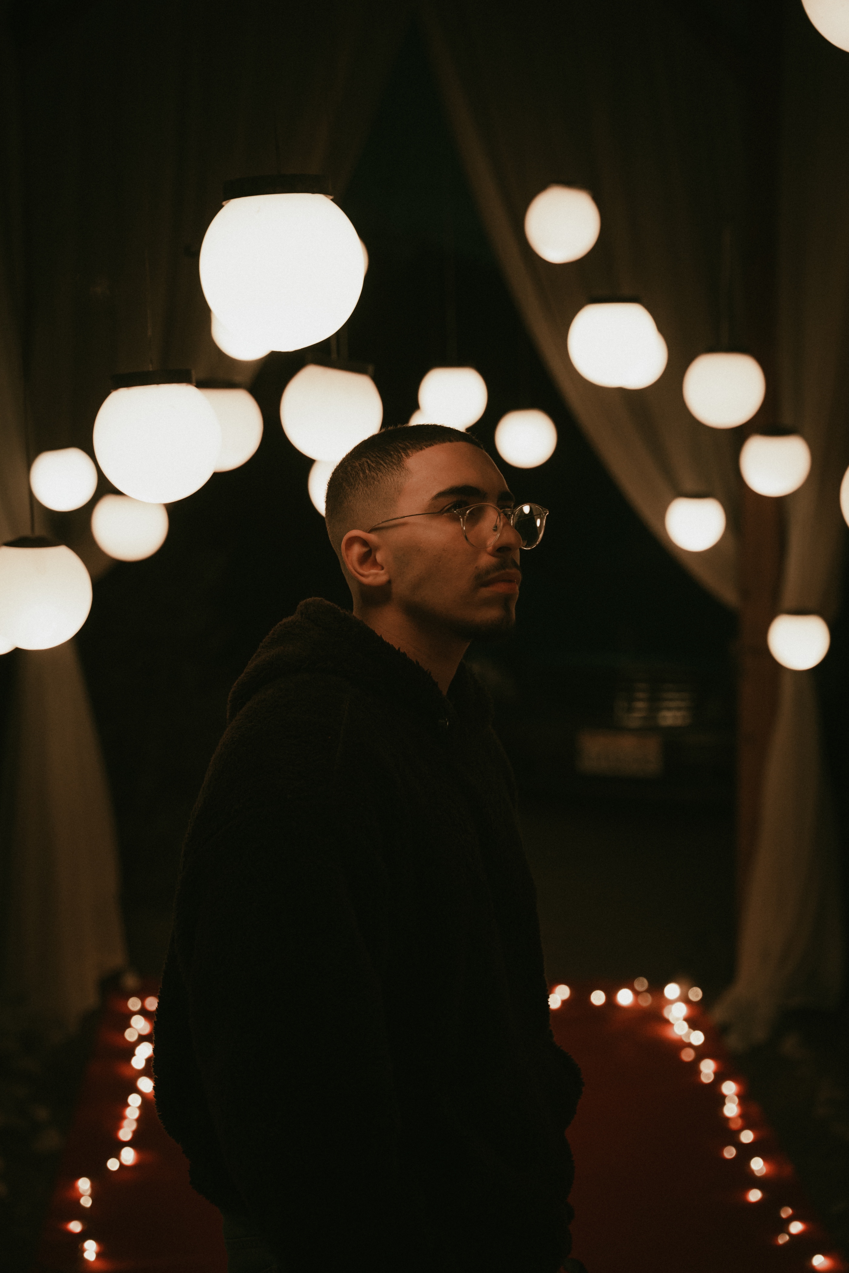 Omar Ramy in profile beneath warm hanging lights